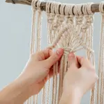 Mains réalisant des nœuds de macramé sur une branche.